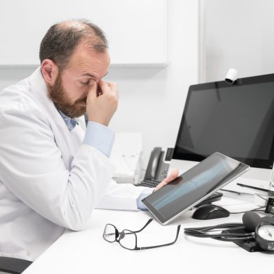 Young doctor rubbing his eyes, feeling tired and unhappy. Health care worker stress and frustration concept. High quality photography